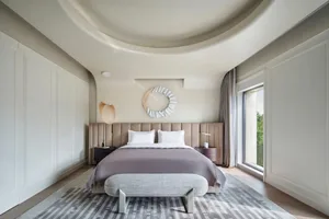 Modern minimalist bedroom with a cozy bed, decorative mirror, and large window.