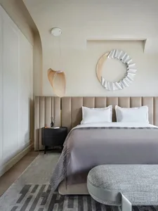 A modern minimalist bedroom with a concrete floor, textured fabric upholstered bed headboard, and a white pendant light fixtu