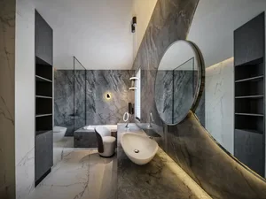 Modern bathroom with marble finishes, featuring a round mirror, sink, and bathtub.