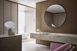 A modern bathroom with a large round mirror, marble sink, wooden panels, and a freestanding bathtub.
