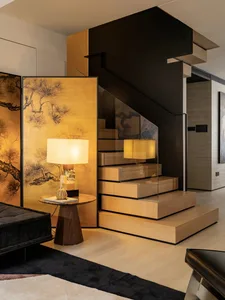 Modern living room with wooden stairs and a table with a lamp and a pumpkin-shaped object.