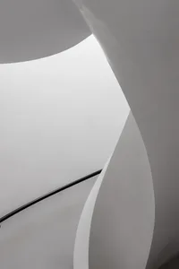 Curved white concrete stairs with a black handrail in a modern interior space.