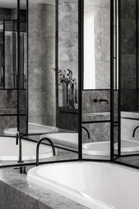 Modern, minimalist bathroom featuring grey marble tiles and a sleek white bathtub.