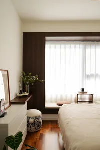 Minimalist bedroom interior with white wood furniture, a large window with sheer curtains, and a bed with a textured blanket.