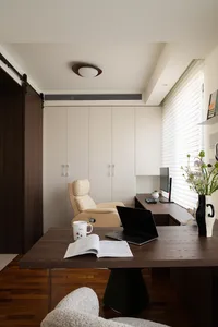 A modern minimalist home office with a wooden desk, beige leather chair, and a window with blinds.
