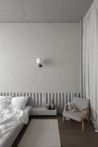 Minimalist bedroom with concrete and wood materials, featuring white bedding and a floating nightstand.