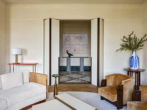 Modern living room featuring white walls, wooden floor, and a white sofa with a side table and lamp, leading to a hallway wit