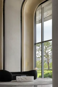 Modern lobby interior with large glass windows displaying outdoor greenery and a sleek, minimalist seating area with marble c