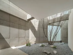 現代極簡室內空間，裸露混凝土牆面搭配礫石庭園，種植稀疏植物與岩石。