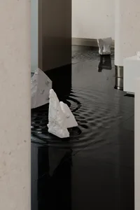 Modern marble interior art installation featuring water flooding on glossy black floor tiles.