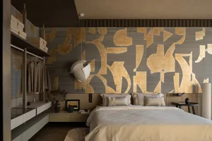 Modern bedroom featuring a patterned wall with abstract shapes in shades of gold and gray, a bed with striped pillows and a r