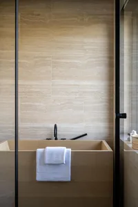 Modern minimalist bathroom with a wooden soaking tub, white towels, and a tiled wall