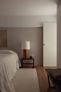 Modern minimalist bedroom featuring wooden furniture with a white lamp and vase.