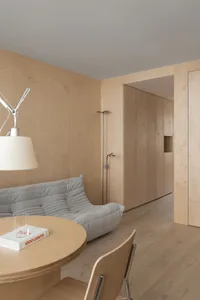 A minimalist living room featuring a grey sofa, round wooden table, and wood-paneled walls.