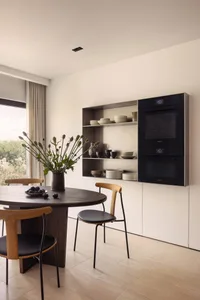 Modern kitchen featuring wooden table and chairs with stainless steel appliances and open shelving.