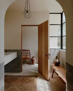 Minimalist bathroom with ceramic tiles, a wooden door, a hanging glass pendant light, and a window with black frames.
