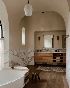 A minimalist bathroom featuring a marble bathtub and sink area with a wooden vanity.