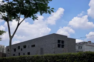 A modern building with a concrete facade and large windows against a blue sky with white clouds.