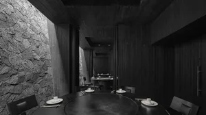 A modern restaurant interior with black tableware, chairs, and a stone wall, featuring a round table and minimalist decor.