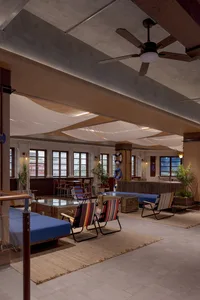A modern industrial-style lobby with exposed concrete ceiling, fabric awnings, and colorful folding chairs.