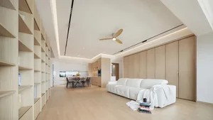 Minimalist living room featuring a white sofa, wooden shelves, and a wooden dining table.