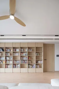 A modern minimalist living room featuring a wall of bookshelves filled with books, a white sofa, and a ceiling fan.
