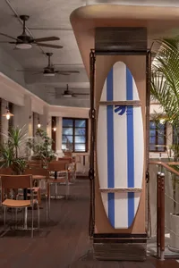 A surfboard decorated with blue stripes and the logo 'Sea Cafe' is mounted in a coastal-themed restaurant interior with woode