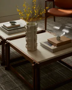 A modern living room with stone and wood tables, books, and a vase with flowers.