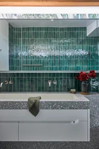 A modern bathroom with green vertical tiles and a concrete countertop, featuring a large bathtub and white cabinets.