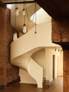 A spiral staircase with white plaster walls and wooden railings and steps