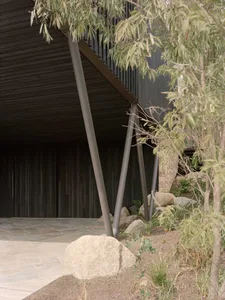 Outdoor minimalist entryway with wooden ceiling and metal frame supported by wooden pillars and surrounded by greenery on a s