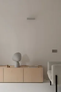 A minimalist living space featuring a sleek, light-colored cabinet with a unique, grey table lamp and a white armchair.