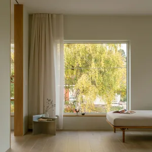 A minimalist bedroom featuring a wood floor, a daybed, and a window with a view of autumn trees.