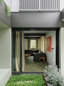 A modern living room with concrete walls and floor, featuring a large sofa, green carpet, and a green plant.