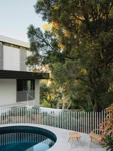 Modern residential exterior with white stucco and glass facade, surrounded by trees and a swimming pool.