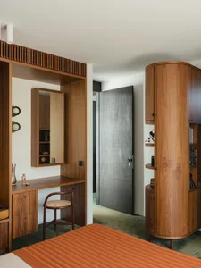 A modern bedroom with wooden furniture including a bed with a striped covering, a vanity with a mirror and a wooden chair.