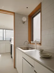 Modern kitchen with white tiled countertops and backsplash, featuring a stainless steel sink and minimalist design.