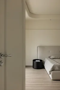 A minimalist bedroom with a grey upholstered bed, black side table, and wooden flooring.