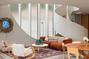 A modern living room featuring an orange couch, white chairs, and a round wooden coffee table.