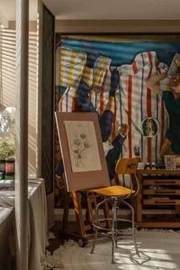 An artist studio with a large mural, easel, and sketch on a canvas.