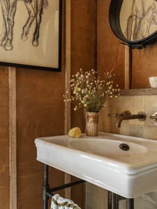 A rustic bathroom interior with a white ceramic sink, a vase of flowers, and wooden panels on the wall.