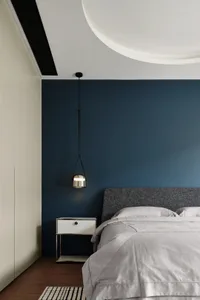 A minimalist bedroom with blue accent wall, grey upholstered bed, metallic bedside lamp, and white nightstand