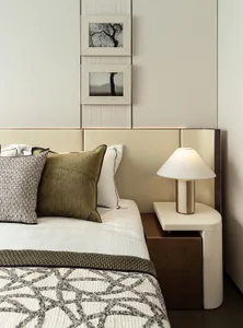 Modern minimalist bedroom with a white leather headboard, green fabric bedding, and beige accents.