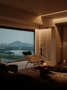 A modern living room with a view of a twilight cityscape and mountains, featuring a comfortable lounge chair, plush cushions,