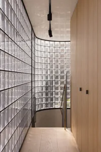 A modern staircase with transparent glass blocks leading downward, bordered by wooden panels and illuminated by overhead ligh