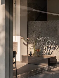 Modern living room featuring a sleek, black coffee table with concrete walls and a large floor vase with flowers.
