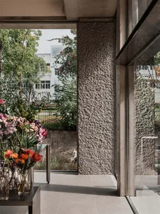 Modern lobby with concrete walls and large windows, featuring a vase of flowers and greenery.