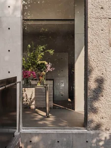 Glass door with concrete columns and floral arrangements inside a minimalist-designed storefront.