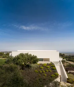 A modern house with a white concrete exterior on a hillside.
