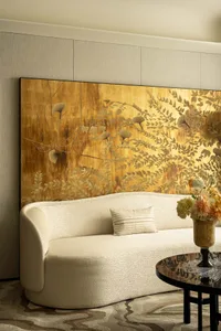 Modern living room with a white sofa, gold wall art, and floral centerpiece on a circular wooden coffee table.